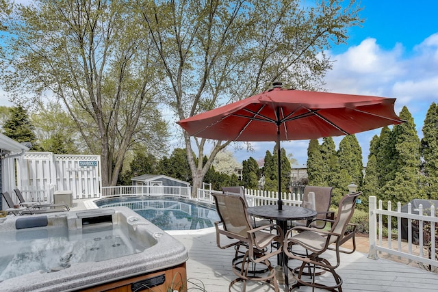 wooden terrace featuring a hot tub, fence, a fenced in pool, an outdoor structure, and outdoor dining space