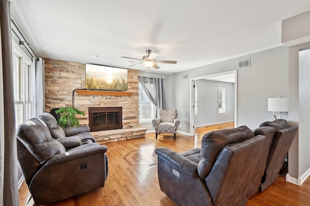 living room featuring ceiling fan, light wood finished floors, a stone fireplace, and visible vents