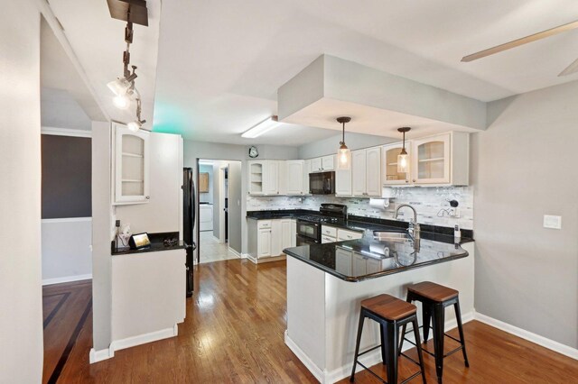 kitchen with decorative backsplash, a peninsula, glass insert cabinets, a kitchen bar, and black appliances