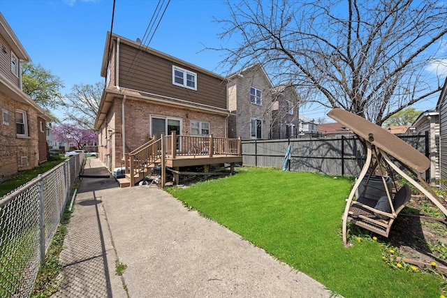 rear view of house featuring a lawn, brick siding, a wooden deck, and a fenced backyard