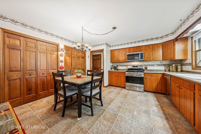 1525 Swallow St, Naperville, IL 60565 - kitchen featuring stainless steel appliances, a chandelier, brown cabinetry, tasteful backsplash, and stone finish floors