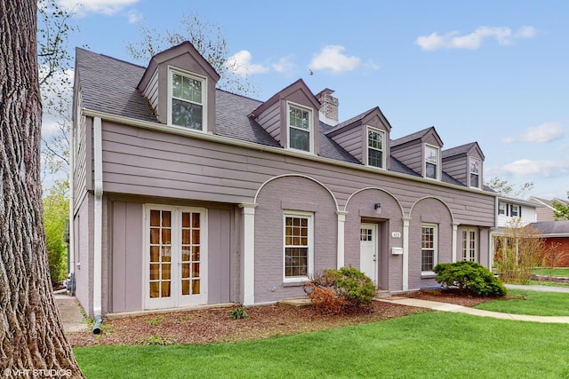 cape cod-style house with a chimney, brick siding, and a front yard