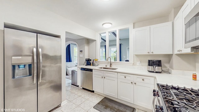 kitchen with light countertops, white cabinets, a sink, appliances with stainless steel finishes, and light tile patterned floors