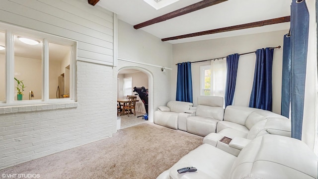 living room featuring carpet floors, arched walkways, beamed ceiling, and brick wall
