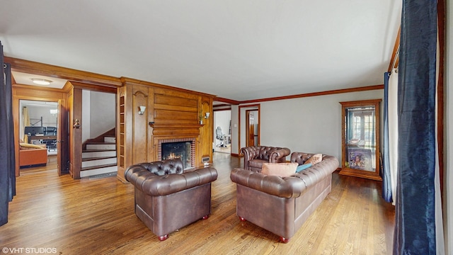 living area with crown molding, stairway, a fireplace, and light wood-type flooring