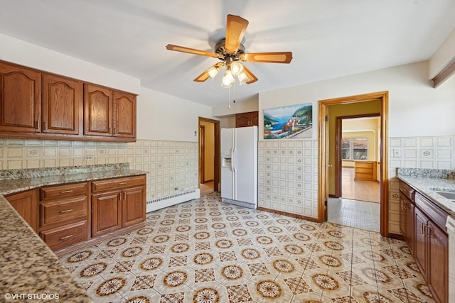 7010 W Devon Ave, Chicago, IL 60631 - kitchen featuring white fridge with ice dispenser, a baseboard heating unit, brown cabinets, light stone counters, and tile walls