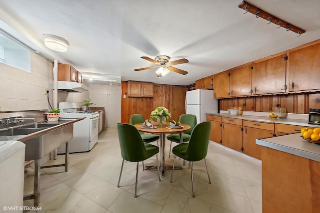 7010 W Devon Ave, Chicago, IL 60631 - kitchen featuring white appliances, under cabinet range hood, a ceiling fan, brown cabinetry, and wood walls