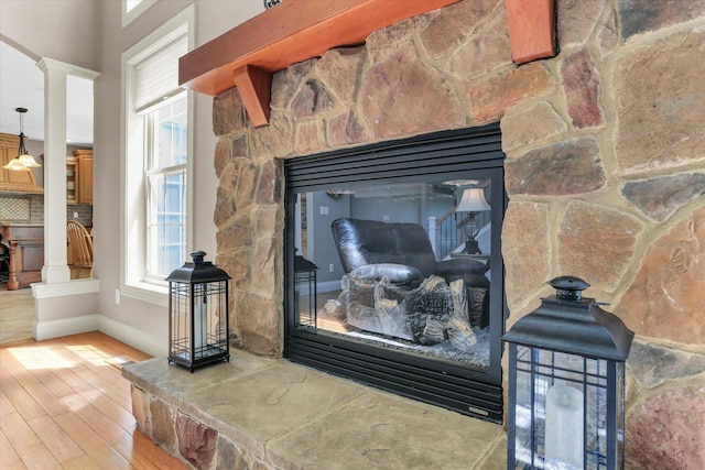 detailed view of a stone fireplace, wood finished floors, ornate columns, and baseboards