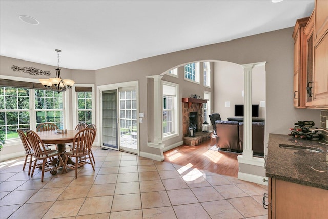 dining area with ornate columns, light tile patterned floors, a fireplace, a chandelier, and arched walkways