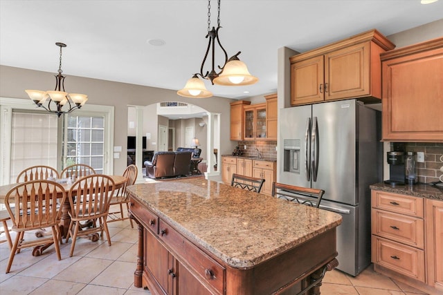 kitchen featuring stainless steel fridge with ice dispenser, tasteful backsplash, a center island, light tile patterned floors, and light stone countertops