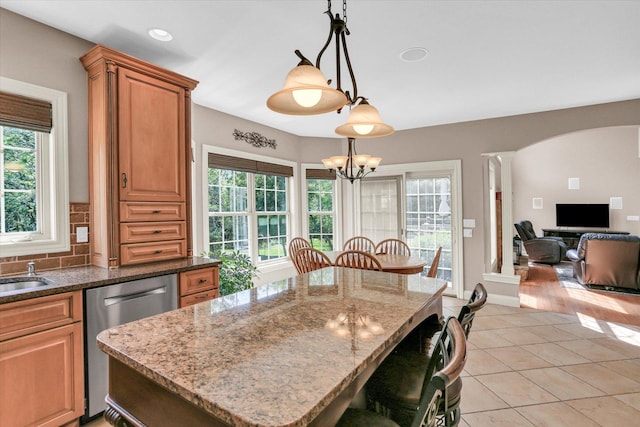 kitchen featuring dishwasher, a chandelier, arched walkways, light tile patterned floors, and dark stone countertops