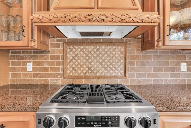 kitchen featuring stainless steel gas stove, tasteful backsplash, exhaust hood, and glass insert cabinets