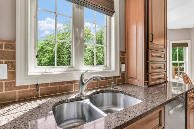 kitchen featuring a sink, plenty of natural light, decorative backsplash, and dark stone counters