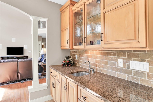 kitchen with a sink, tasteful backsplash, stone counters, decorative columns, and glass insert cabinets