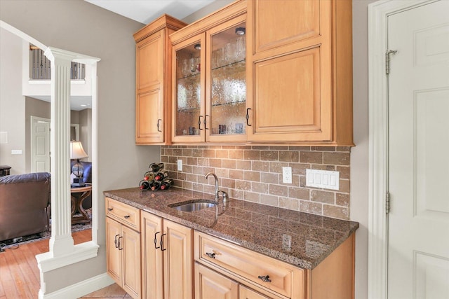 kitchen featuring a sink, decorative columns, decorative backsplash, and dark stone counters