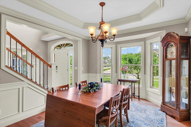 dining space featuring stairs, a chandelier, a wainscoted wall, a decorative wall, and light wood-style flooring