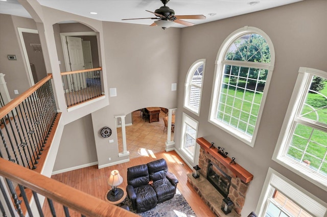 living room with arched walkways, healthy amount of natural light, ceiling fan, a fireplace, and a towering ceiling