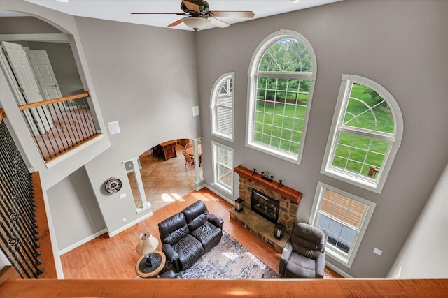living area featuring a towering ceiling, ceiling fan, arched walkways, wood finished floors, and a stone fireplace