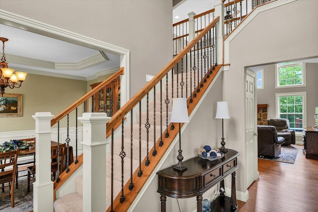 staircase with a high ceiling, wood finished floors, a chandelier, ornamental molding, and baseboards