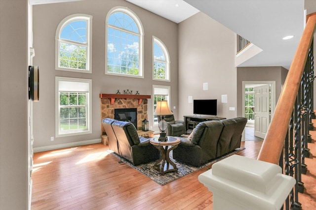 living area with a stone fireplace, light wood-type flooring, stairway, a towering ceiling, and baseboards