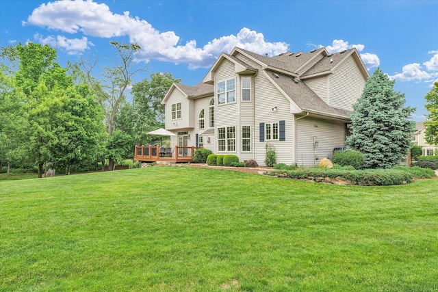 rear view of property featuring a shingled roof, a wooden deck, and a lawn