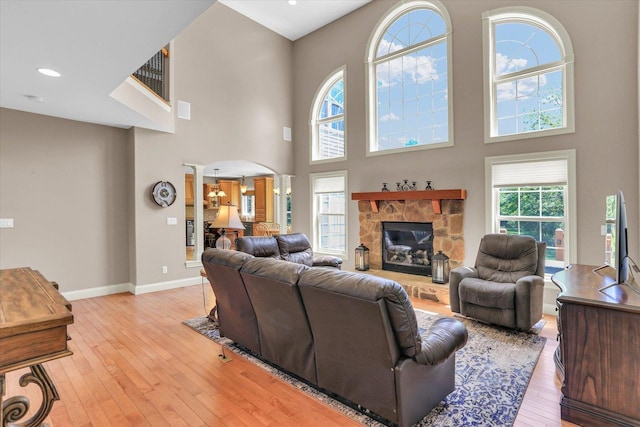 living room featuring light wood-style flooring, ornate columns, baseboards, arched walkways, and a fireplace