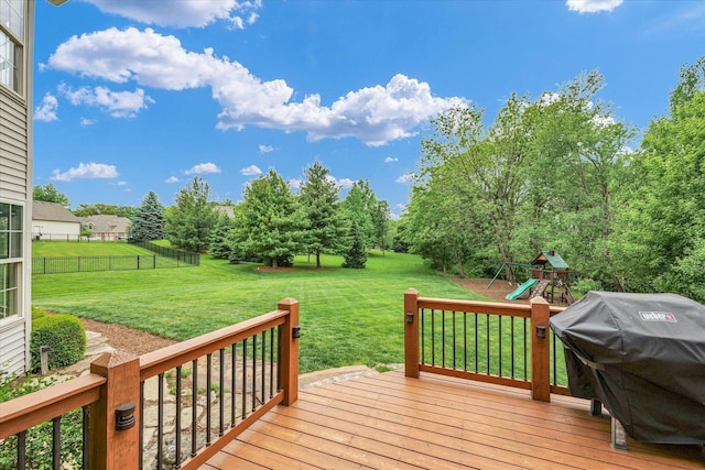 deck with a grill, a playground, and view of wooded area