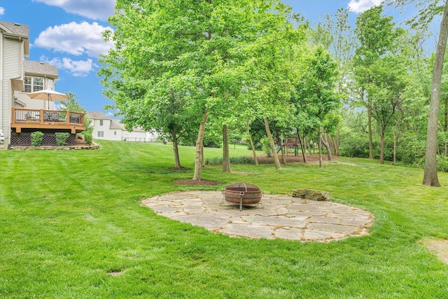 view of grassy yard with an outdoor fire pit, a wooden deck, a playground, and a patio area