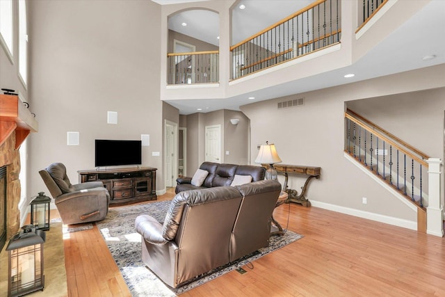 living room featuring a towering ceiling, hardwood / wood-style flooring, a stone fireplace, stairs, and baseboards