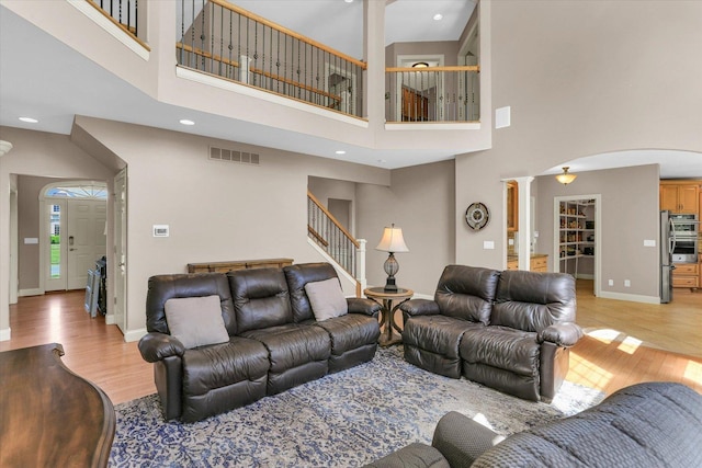 living room with decorative columns, light wood finished floors, stairway, baseboards, and a towering ceiling