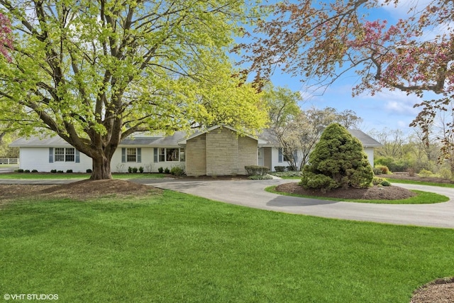 ranch-style home with driveway, a front lawn, and stone siding