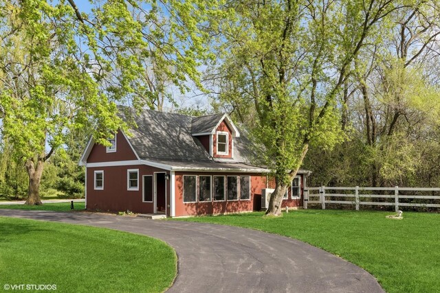 view of front of home with a shingled roof, a front lawn, fence, and driveway
