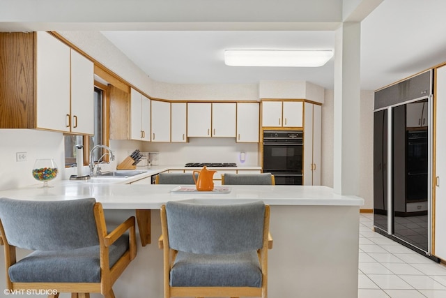 kitchen featuring a kitchen bar, a sink, light countertops, light tile patterned floors, and a peninsula