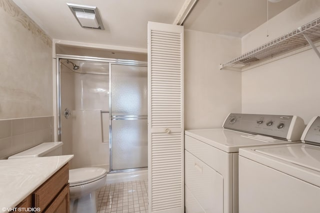 washroom featuring laundry area, visible vents, washing machine and clothes dryer, tile walls, and light tile patterned flooring