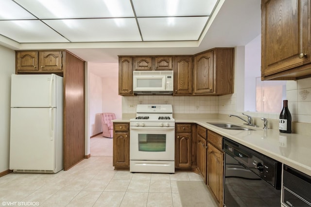 kitchen with tasteful backsplash, brown cabinets, a sink, light countertops, and white appliances