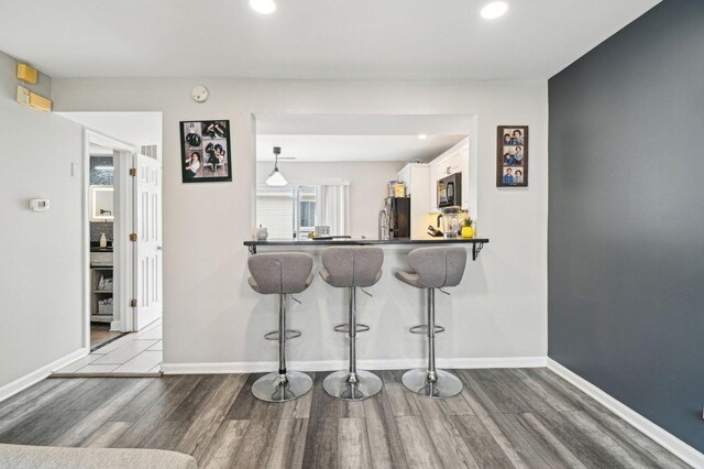 kitchen featuring black microwave, freestanding refrigerator, a kitchen bar, and wood finished floors
