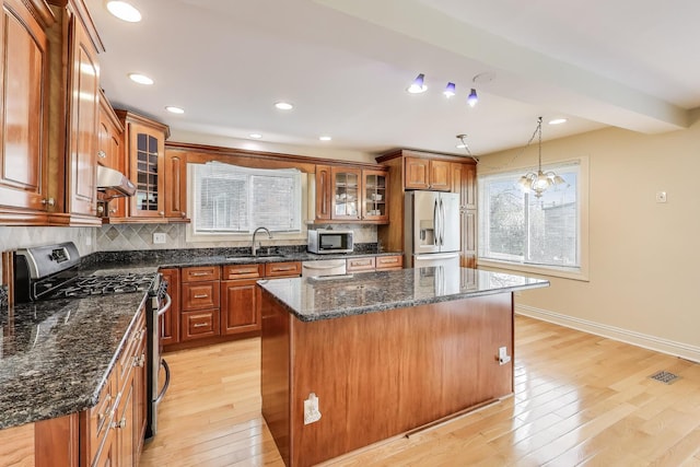 kitchen featuring brown cabinets, light wood-type flooring, a sink, under cabinet range hood, and stainless steel appliances