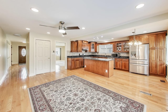 kitchen with backsplash, a kitchen island, appliances with stainless steel finishes, light wood-type flooring, and brown cabinets