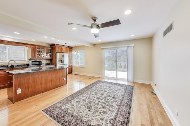 kitchen with appliances with stainless steel finishes, a sink, a center island, visible vents, and glass insert cabinets