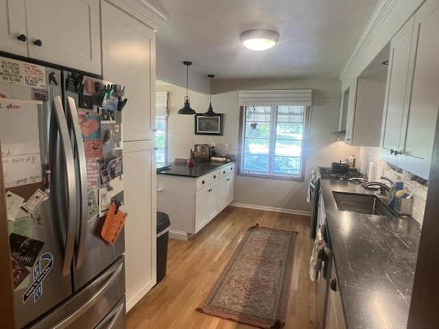 kitchen featuring stainless steel appliances, a sink, light wood-type flooring, dark countertops, and white cabinets