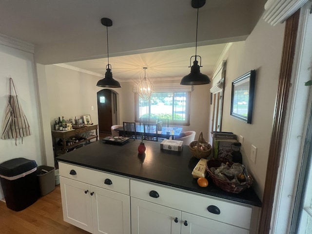 kitchen featuring dark countertops, crown molding, light wood-style floors, white cabinets, and decorative light fixtures