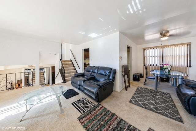 living area with carpet floors, stairs, and ceiling fan
