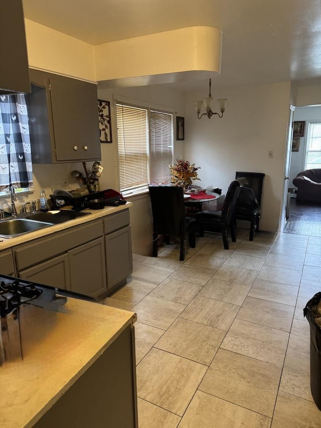 kitchen featuring an inviting chandelier, light countertops, a sink, light tile patterned floors, and gray cabinetry