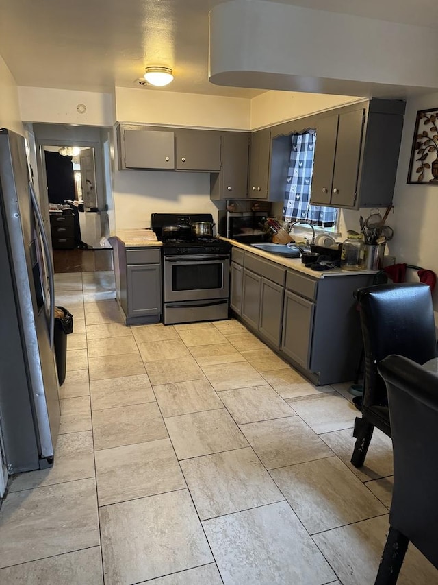 kitchen featuring appliances with stainless steel finishes, a sink, light countertops, light tile patterned floors, and gray cabinetry