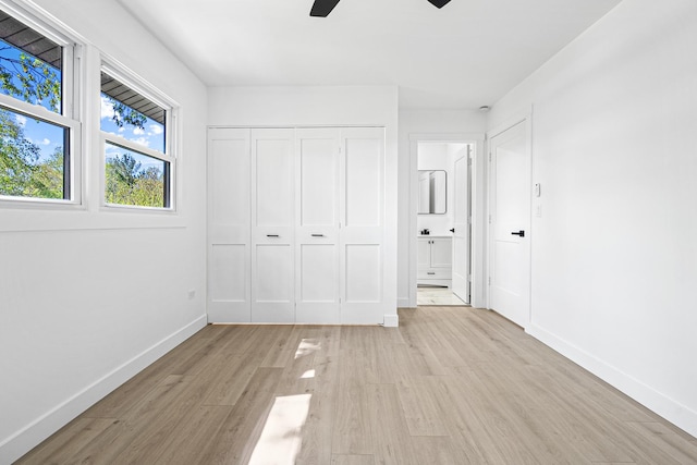 unfurnished bedroom with light wood finished floors, baseboards, ensuite bathroom, ceiling fan, and a closet