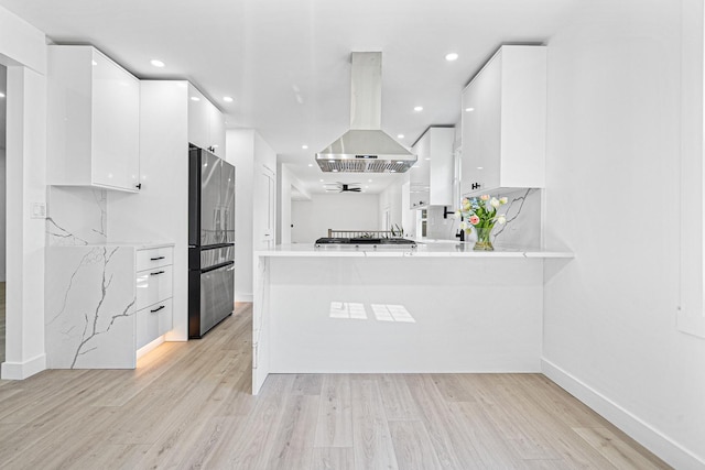 kitchen with freestanding refrigerator, island range hood, modern cabinets, white cabinets, and light wood finished floors