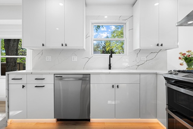 kitchen with stainless steel appliances, wall chimney range hood, and white cabinets