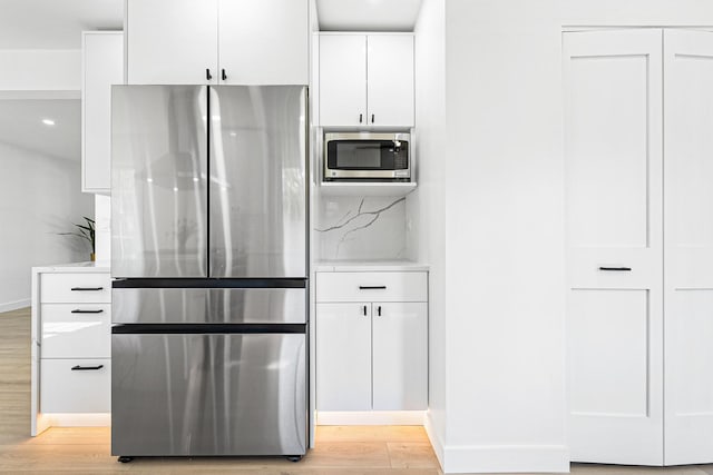 kitchen with appliances with stainless steel finishes, light wood finished floors, white cabinets, light countertops, and baseboards