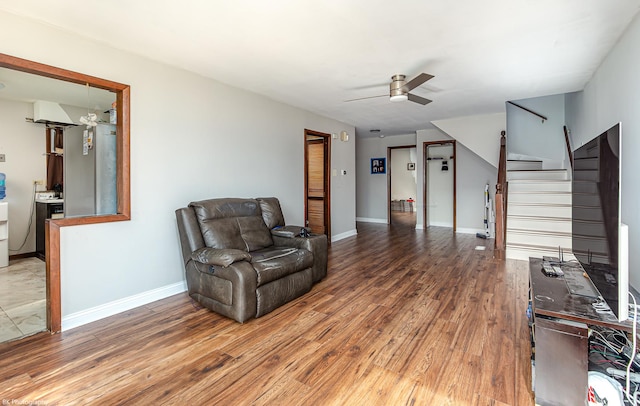 sitting room featuring stairway, baseboards, a ceiling fan, and wood finished floors