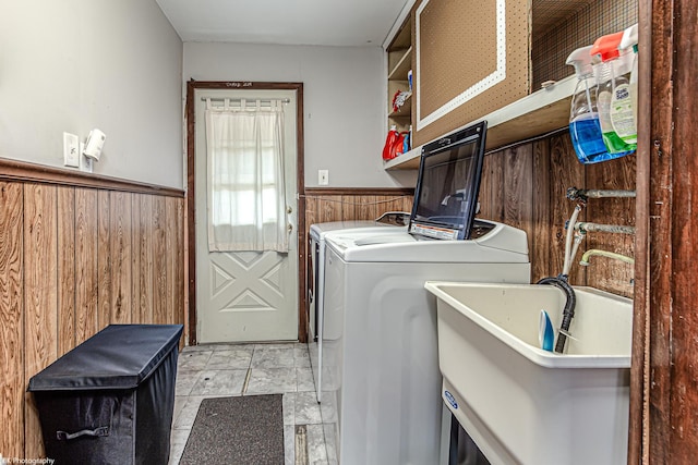 laundry area with laundry area, wainscoting, wooden walls, washing machine and clothes dryer, and a sink